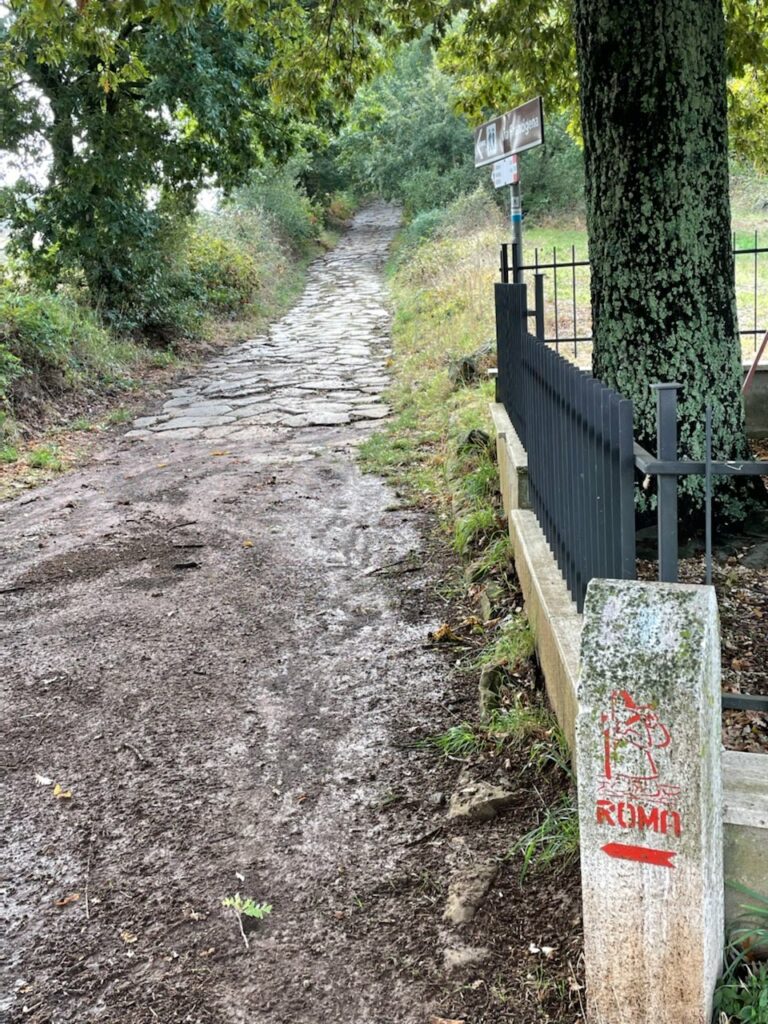 Dirt and stone road with Rome sign and trees.